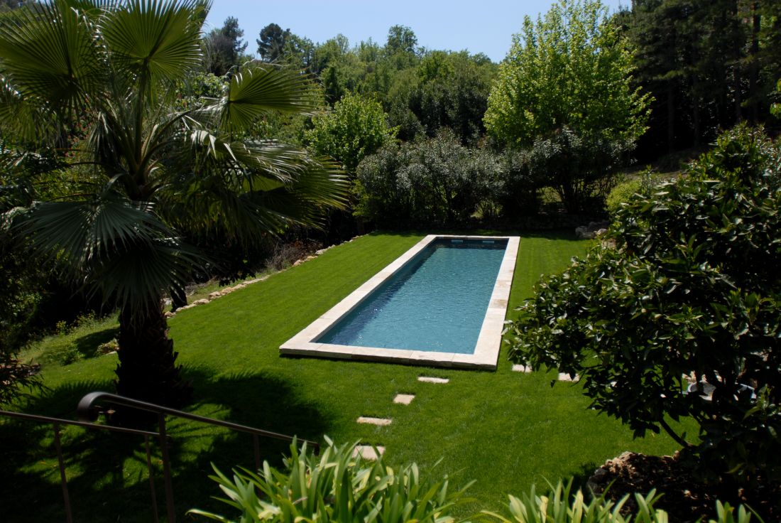 A traditional lap pool with a beautiful natural stone border and slate-grey liner in the middle of a lush green lawn.