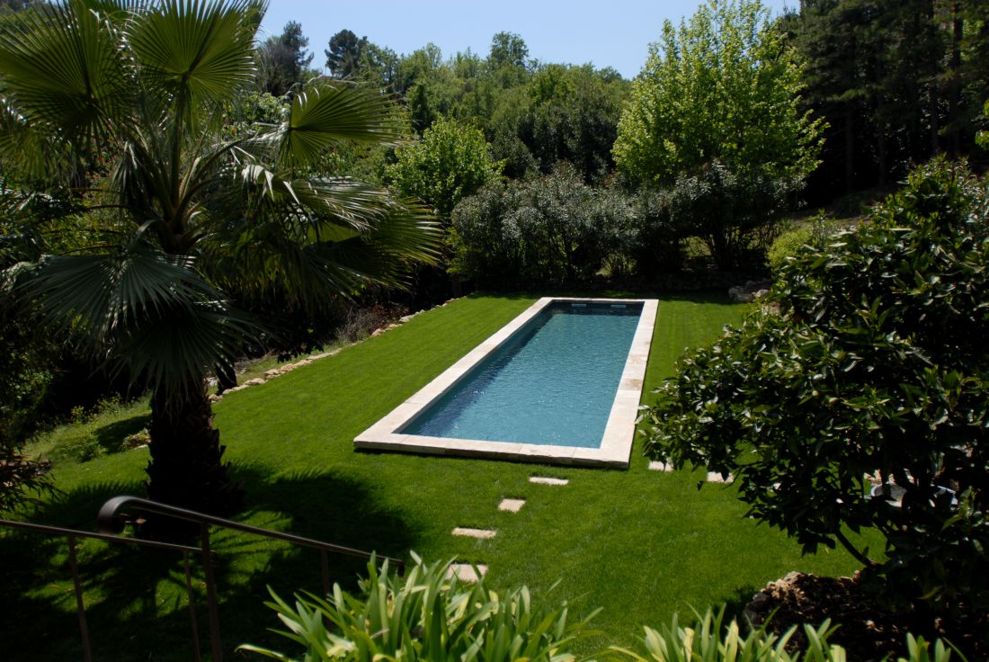 Piscine en forme de bassin de nage traditionnel équipé d'une belle margelle en pierre naturelle et d'un liner gris ardoise au milieu d'un gazon verdoyant.