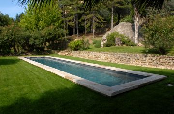 La margelle en pierre naturelle et la couleur de l'eau donnent un aspect bassin traditionnel à cette piscine contemporaine.