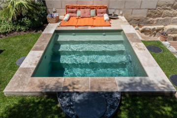 Petite piscine carrée avec margelle en pierre de travertin et liner vert argile.