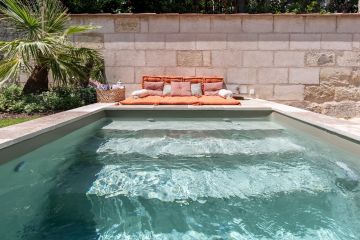 Au pied du mur en pierre naturelle, la piscine a été pensée comme un prolongement du bâti existant, avec des surfaces de dallage dans la même tonalité de couleur.