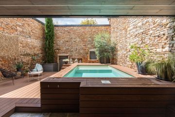 Parfaitement intégré au premier plan, sous la terrasse en bois, est dissimulé le local technique de la piscine. Discret, il fait place à une véritable pièce extérieure tout en déco.