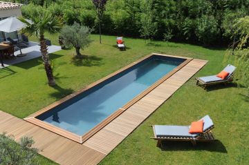 Une piscine couloir de nage CN 10 au milieu d'un jardin entourée d'une pelouse et d'un peu de terrasse en bois