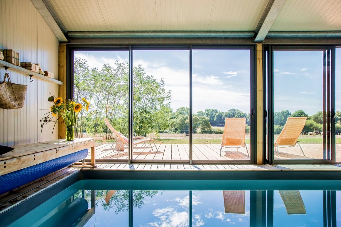 Les larges bais vitrées alignées le long de la piscine sont comme autant de tableaux montrant la campagne angevine. Depuis les canapés à l'intérieur, la piscine se transforme en miroir hypnotique appelant le visiteur de ce gîte à la contemplation.