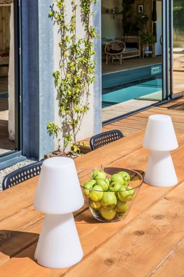 Sur une grande table en bois des lampes d'extérieur et quelques fruits frais pour passer un après-midi et une soirée en été au bord de la piscine.