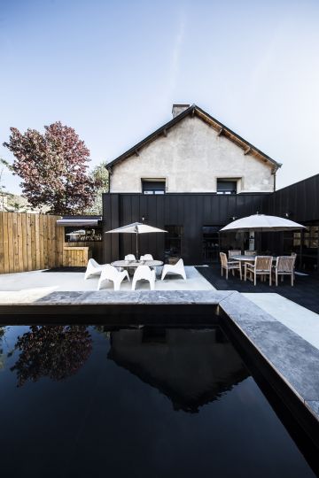 La piscine au premier plan disparaît presque sous l'effet du liner noir qui semble correspondre avec le bardage métallique de la maison moderne.