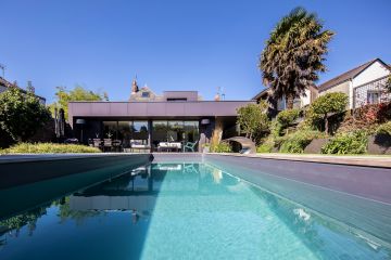 La piscine et son liner gris ardoise sont en harmonie parfaite avec le bardage en zinc de l'extension de maison moderne.