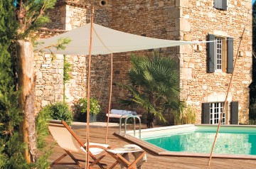 Une piscine Hx avec terrasse en bois devant une grande maison en pierre