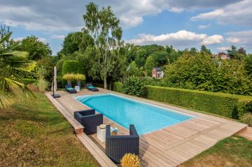 Cette piscine traditionnelle a été réalisée avec une structure autoportante en aluminium double peau breveté Piscinelle et est équipée d'une couverture de sécurité automatique et immergée dissimulée sous un caillebotis intégré à la terrasse.