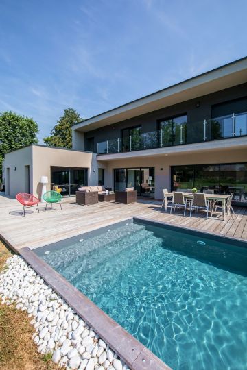 Les galets blancs assurent le lien entre l'étendue de gazon et la margelle de cette piscine contemporaine en Belgique.