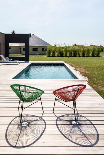 Les fauteuils Acapulco rouge et vert ajoutent une touche de couleur et rehaussent le gris argenté de la terrasse en ipé en donnant du peps à l'ensemble.