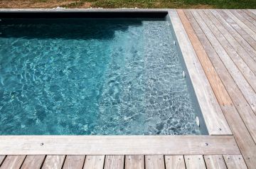 The perfectly treated and filtered water in the pool is crystal-clear, conveying the full depth and colour variation of the slate-grey liner.