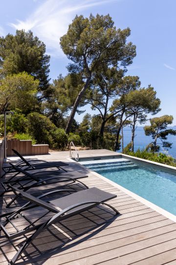 Terrasse bois et transats au bord d'une piscine vue mer - Piscinelle