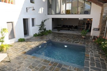 Petite piscine carrée de 10m² entièrement entourée de pierre naturelle jusqu'au bord de l'eau et dans le prolongement du sol de la maison.