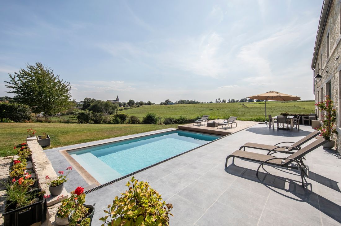 Le projet de rénovation mêle pierre bleu, piscine, bois et gazon pour un tableau d'une esthétique aboutie.